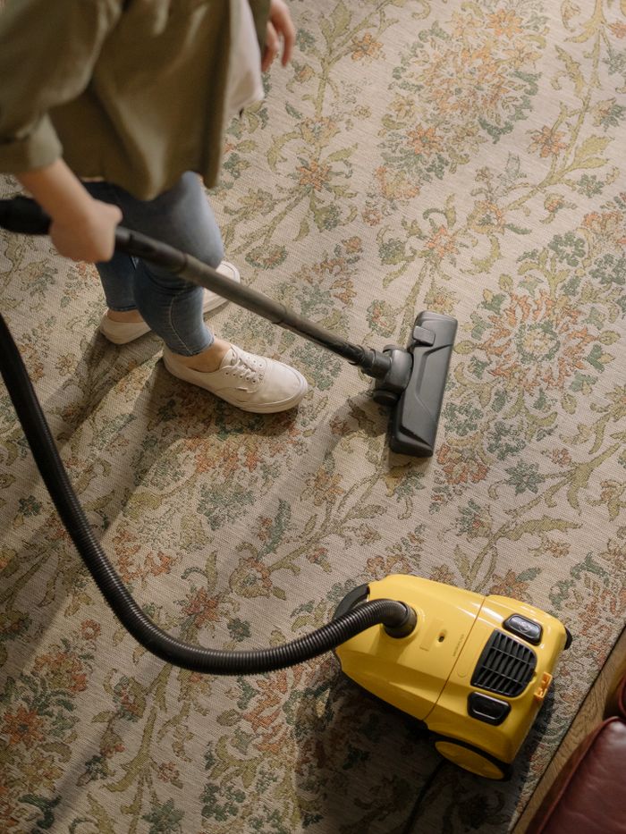 Mastering the First Impression: Your intriguing post title goes here Person cleaning a floral carpet with a yellow vacuum cleaner indoors.